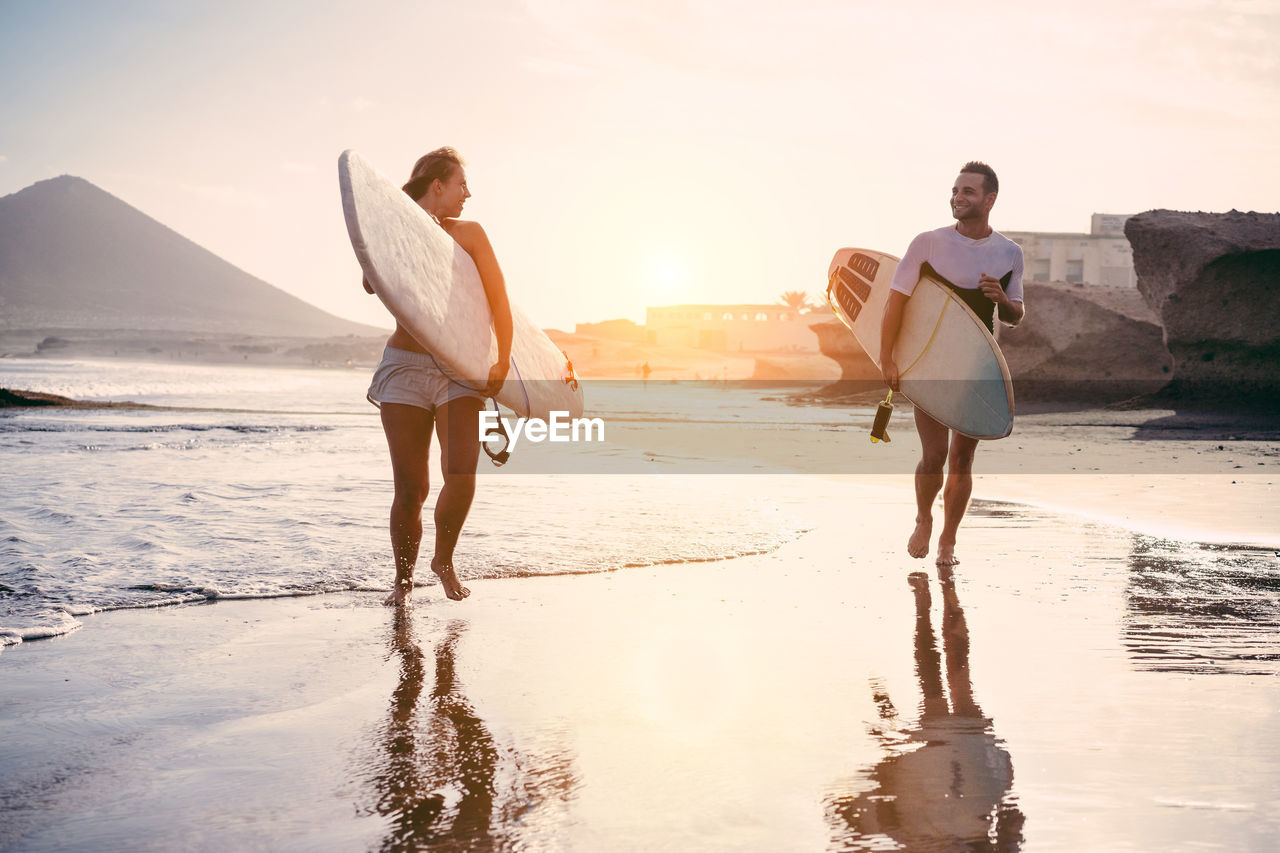 Full length of young couple with surfboard walking on shore at beach