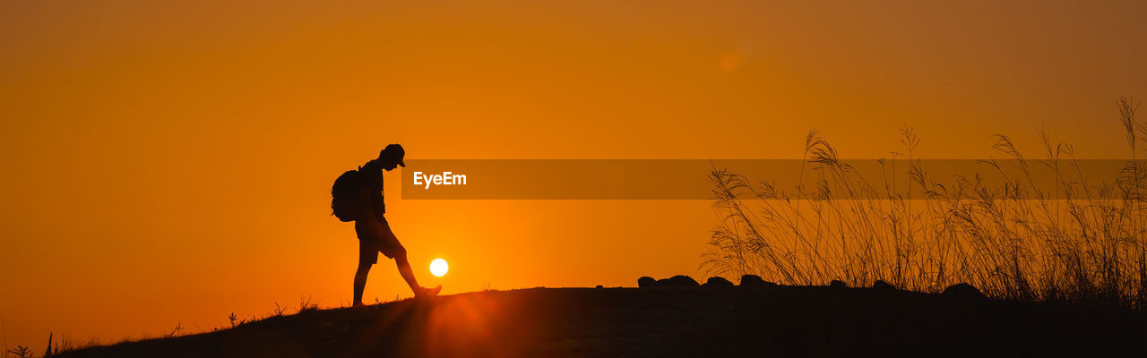 SILHOUETTE MAN STANDING ON LAND AGAINST ORANGE SKY