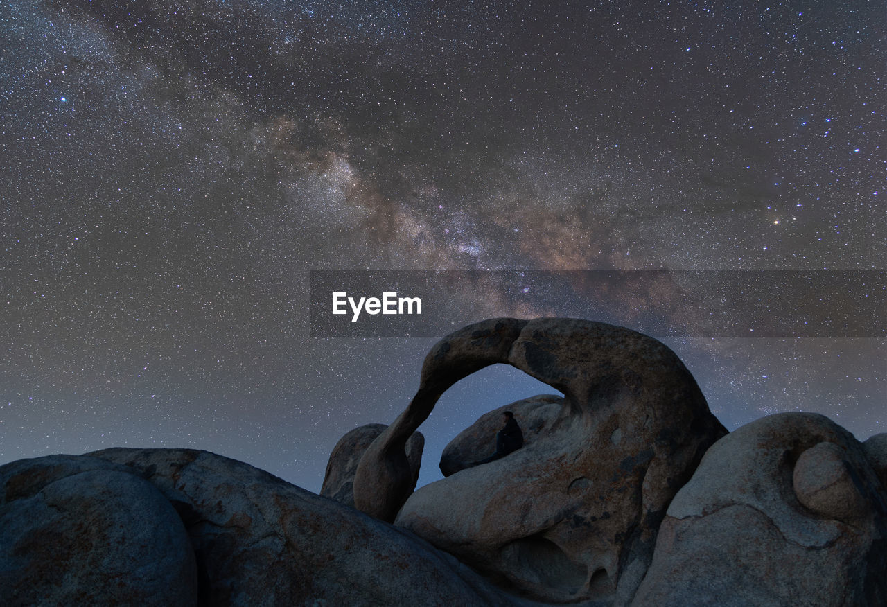 Milky way over mobius arch with a lone man sitting in the arch