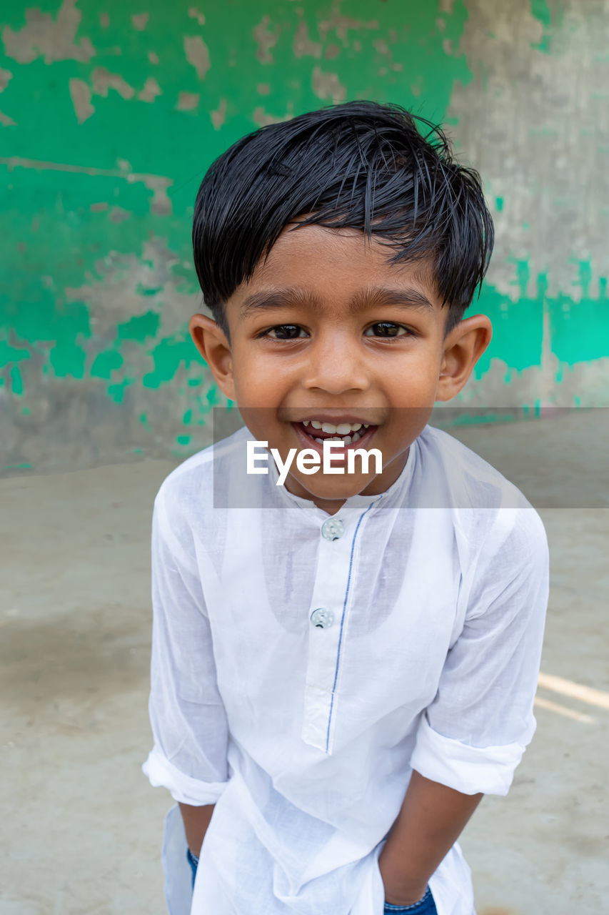 PORTRAIT OF A SMILING BOY STANDING AGAINST WALL