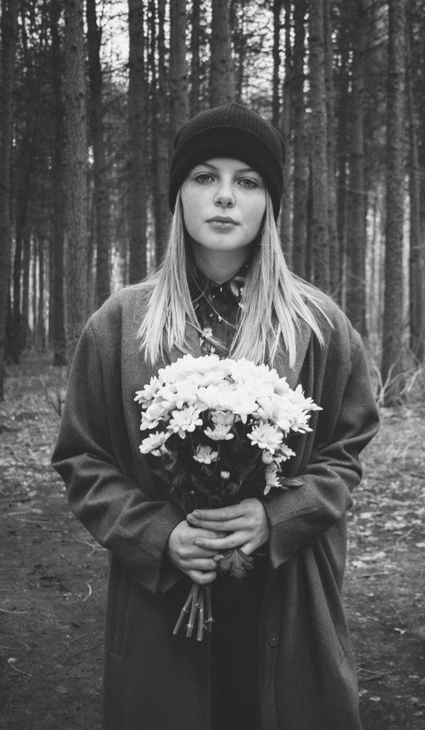 Portrait of a young woman holding bouquet against tree trunks