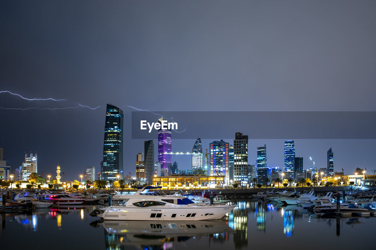 ILLUMINATED MODERN BUILDINGS BY BAY AGAINST SKY