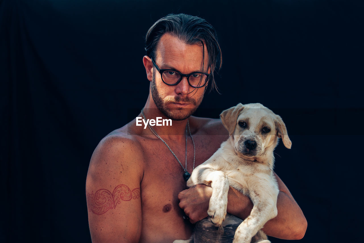 Portrait of man with dog against black background