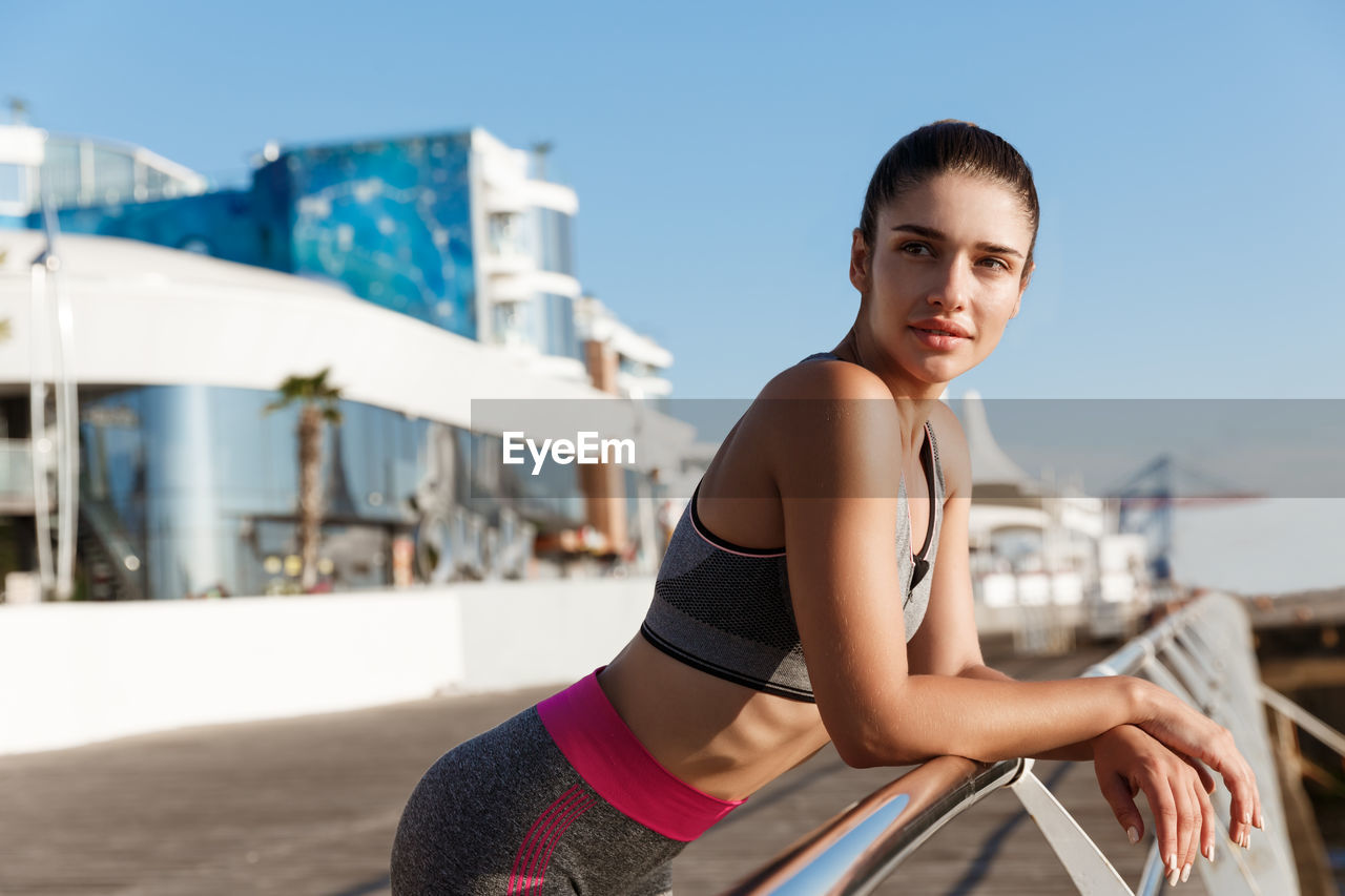 Young woman looking away while leaning on railing against sky