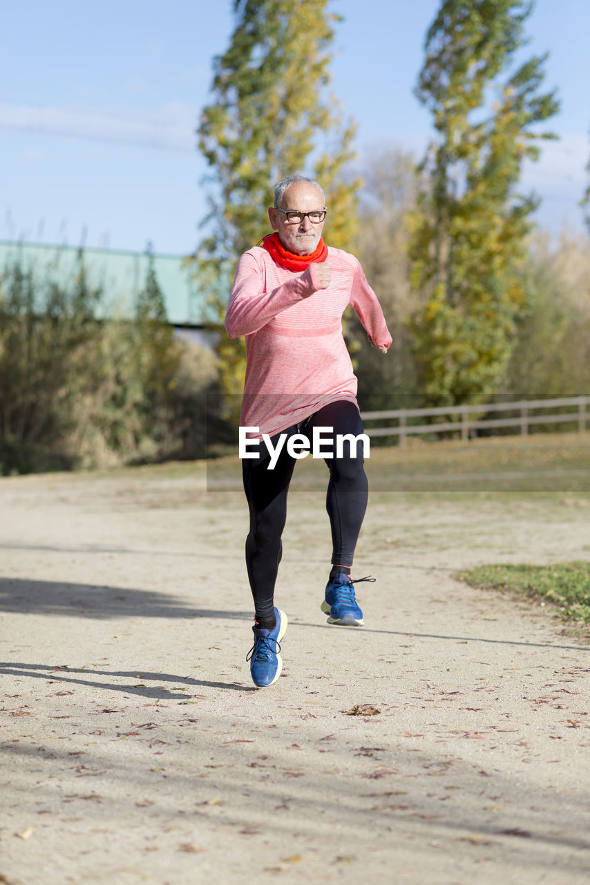 Senior man running on sand against sky