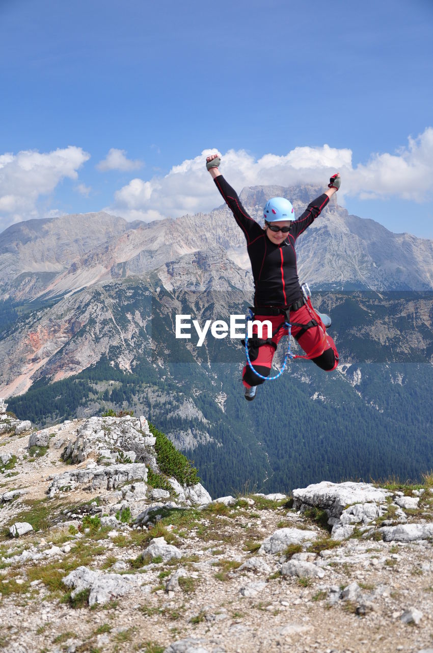 Woman jumping over mountain against sky