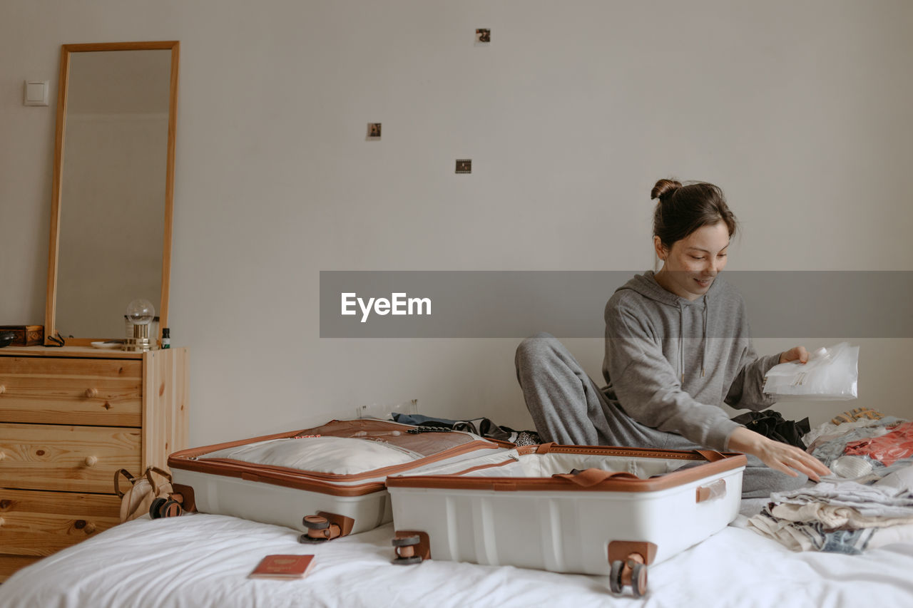 Smiling woman packing her suitcase at home on the white bed