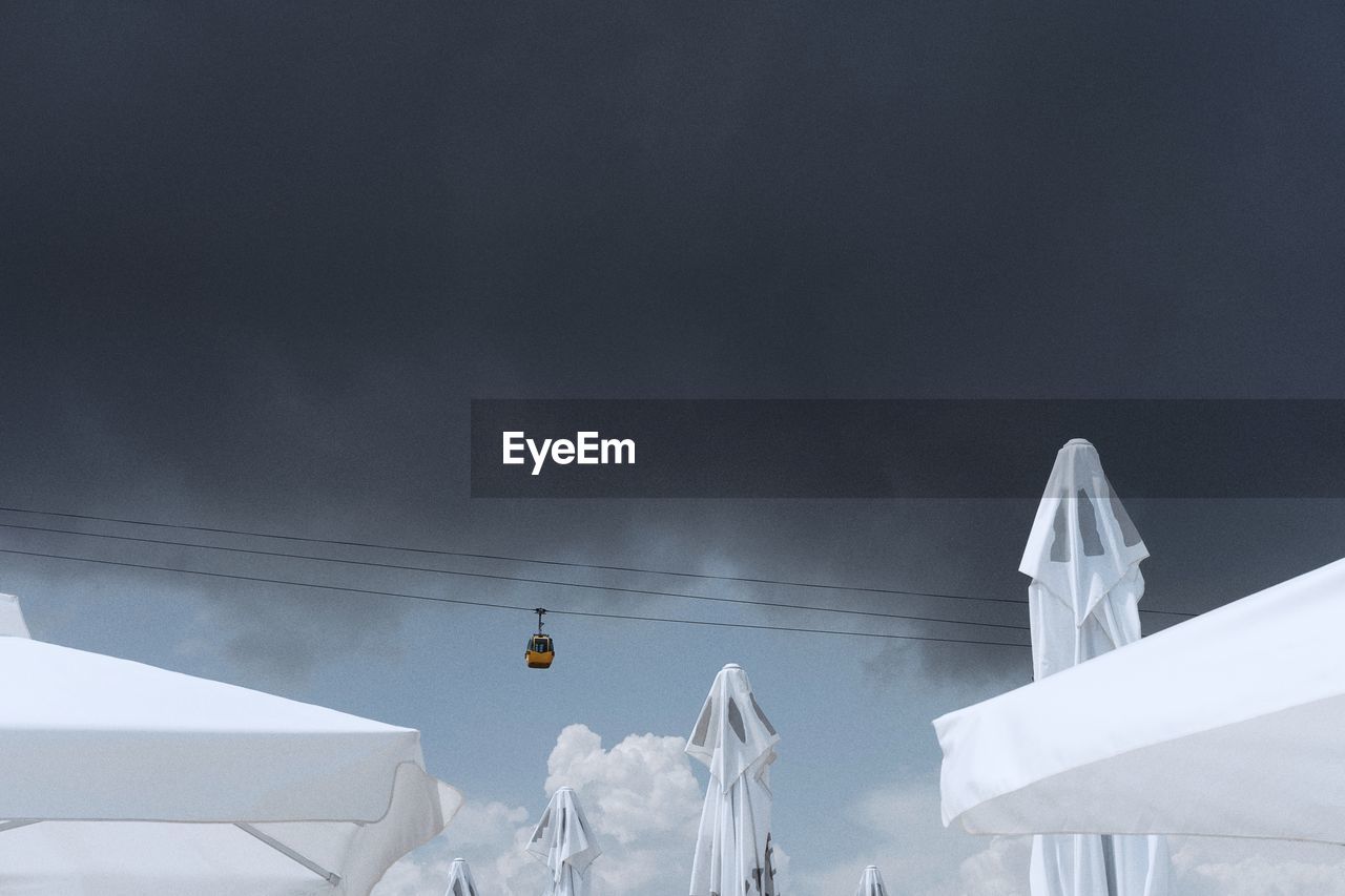 Low angle view of cable car over parasols against cloudy sky