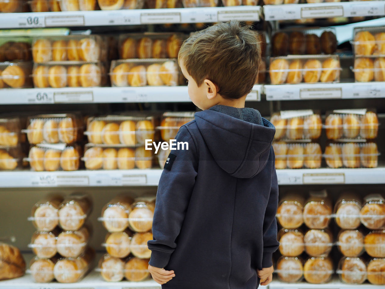 Cute toddler boy in casual clothes in bakery looking at donuts