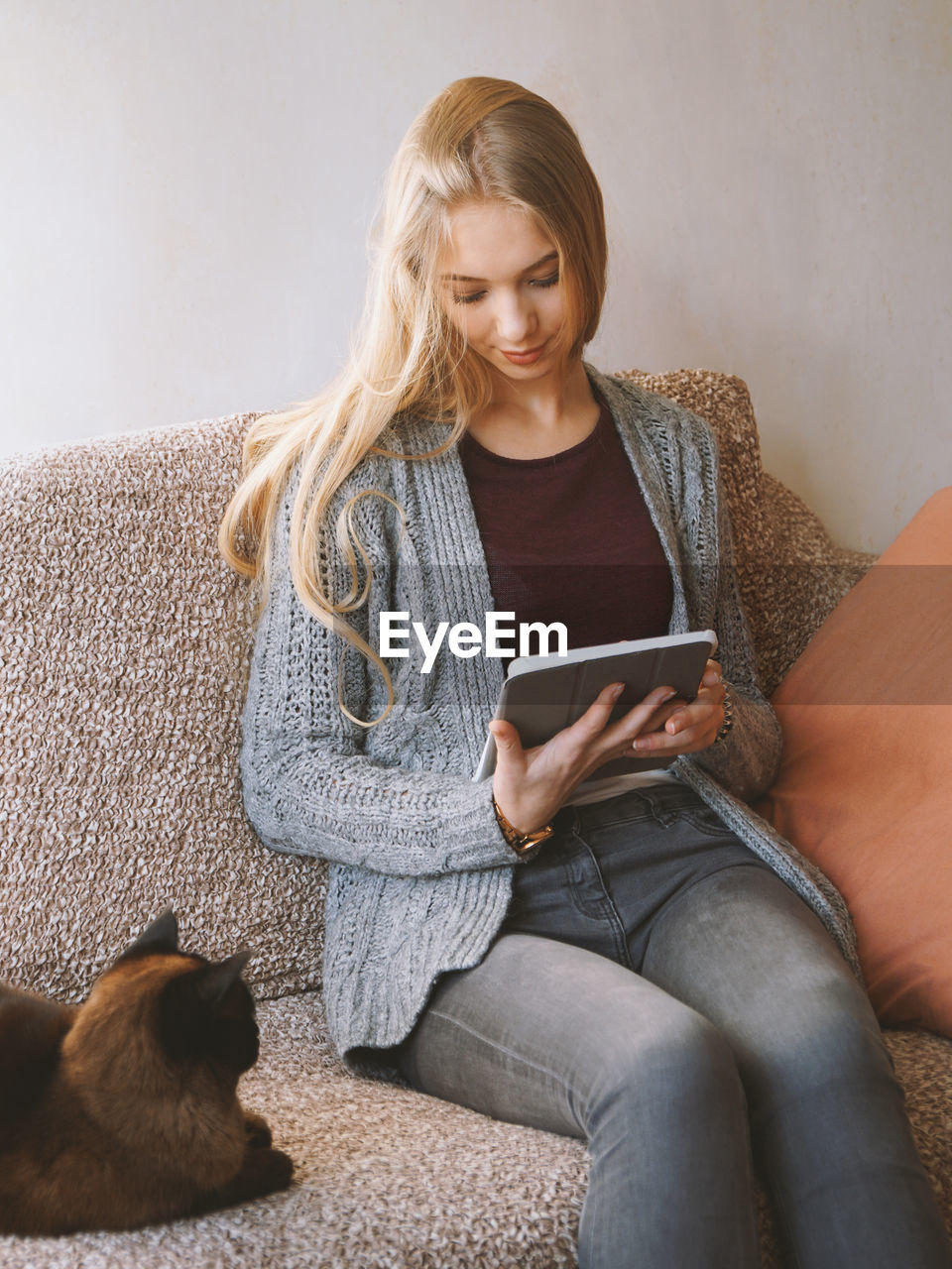 Stay at home teenage girl reading e-book or using tablet computer while sitting on sofa with cat 