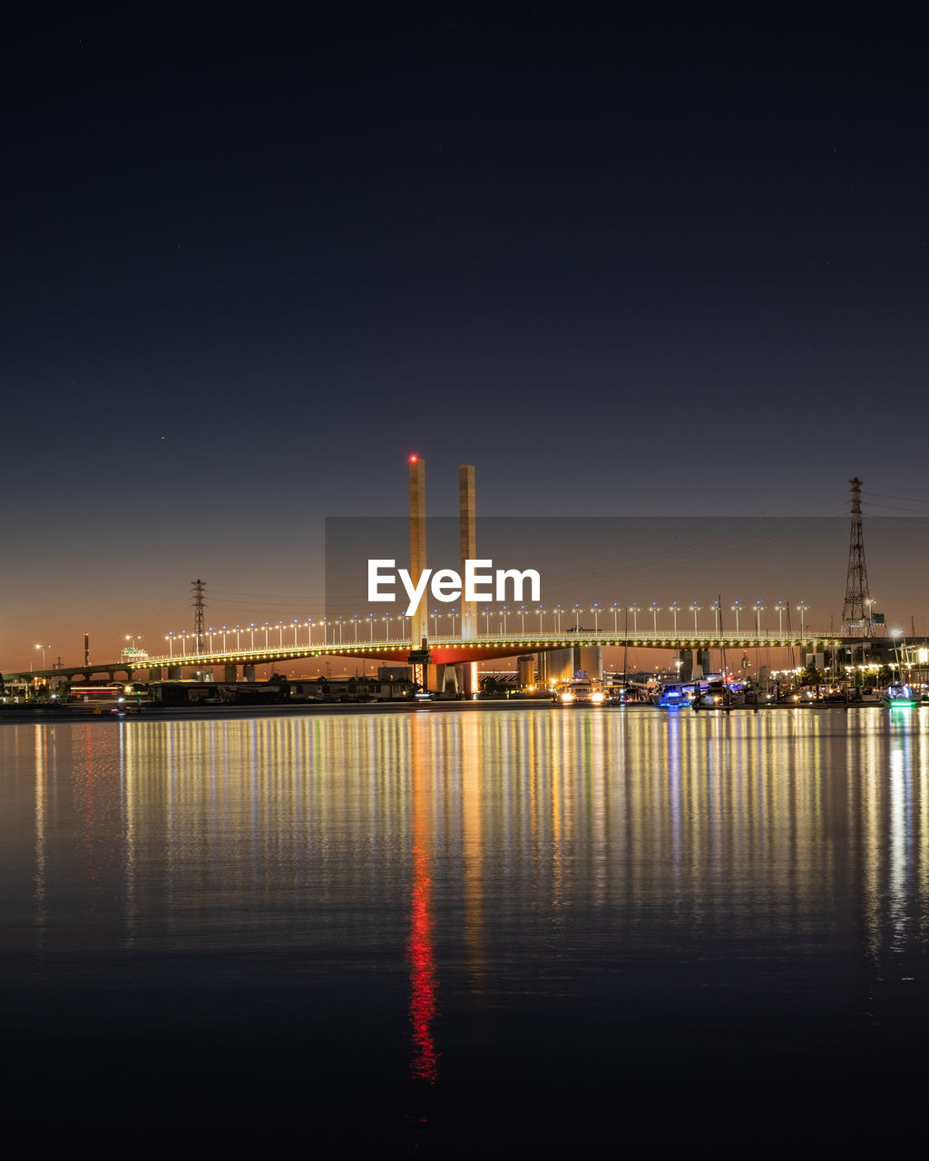 Illuminated city by river against sky at night