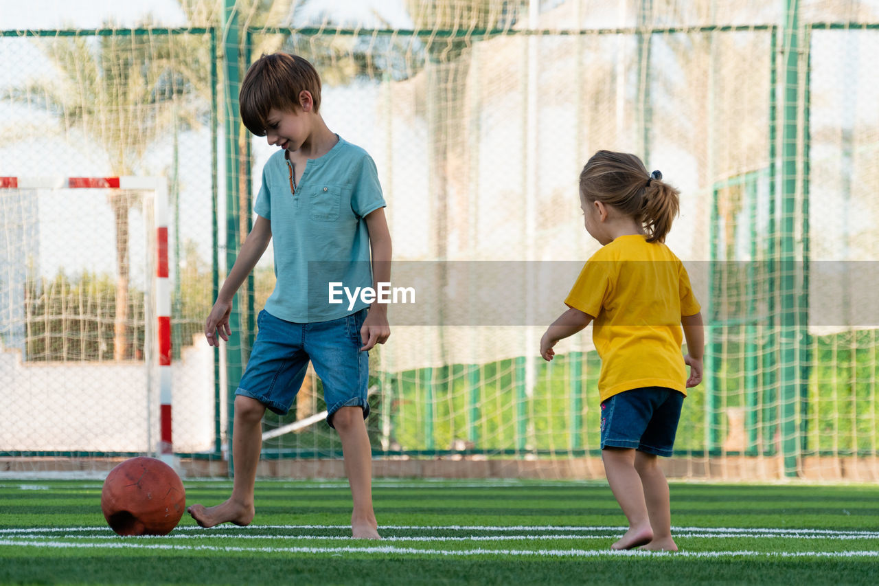 Boy and girl playing football on green sports field.