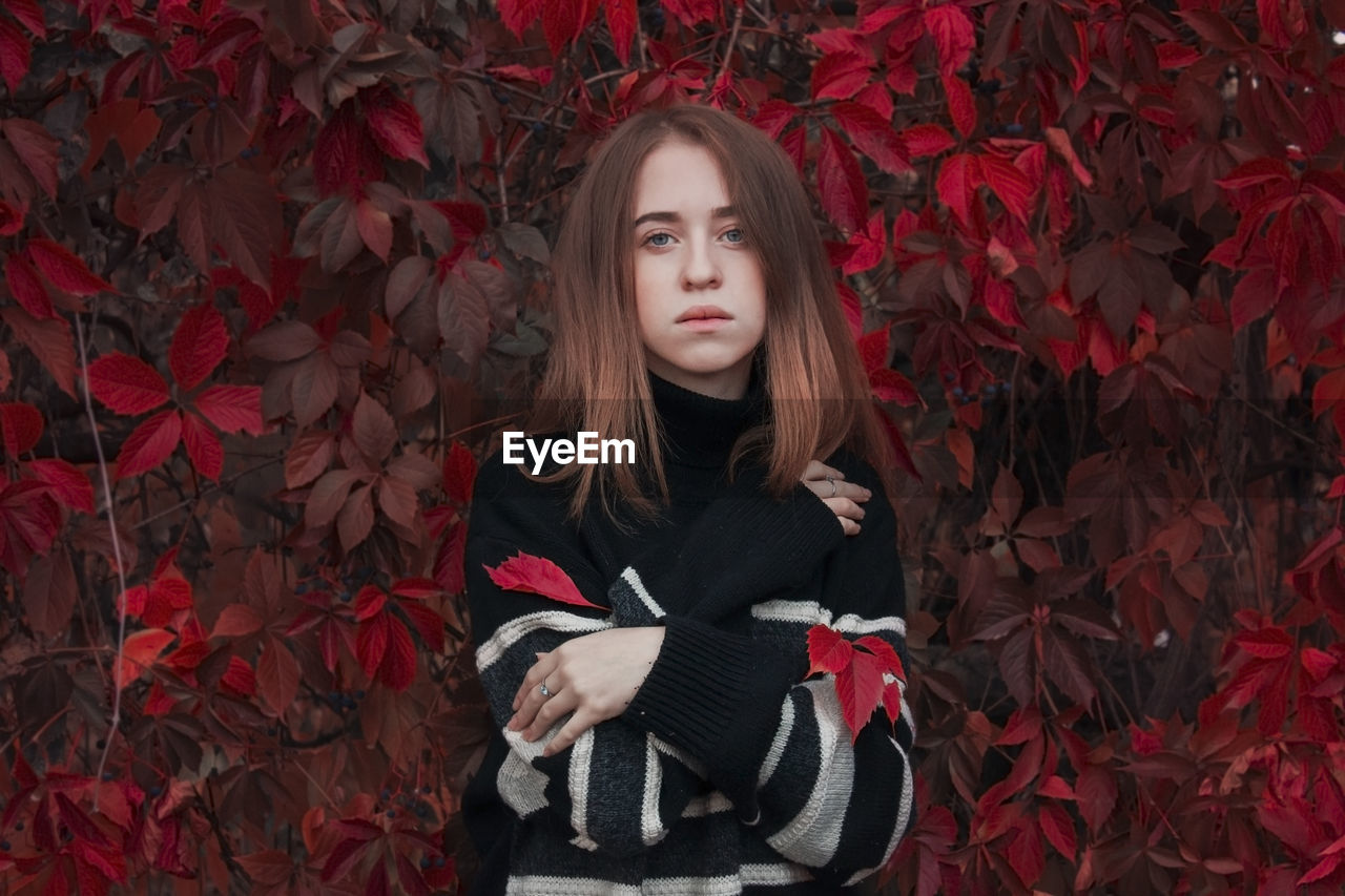 Autumn portrait of a beautiful cute woman against a background of bright red leaves. black sweater