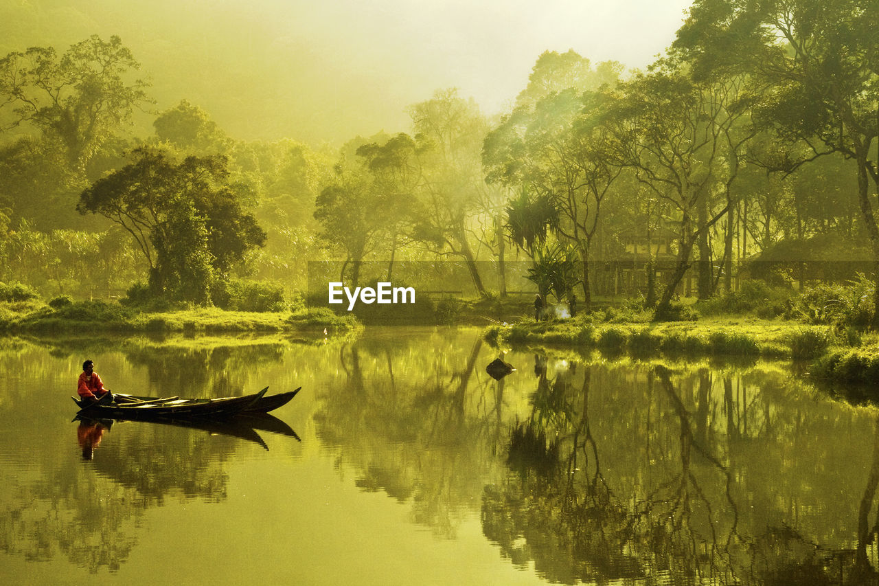 Man sitting on boat in lake against trees