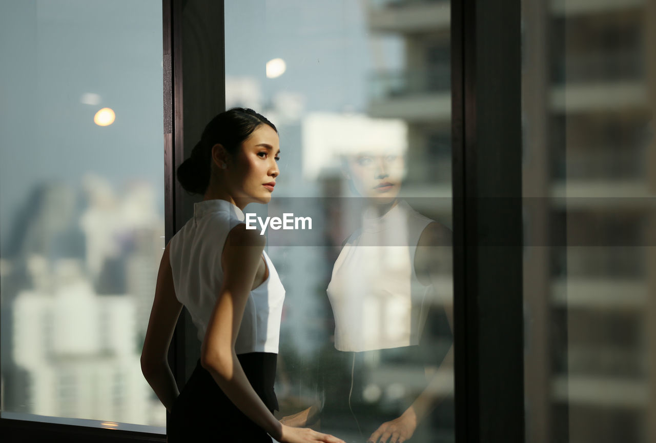 Businesswoman looking away while standing by window at office