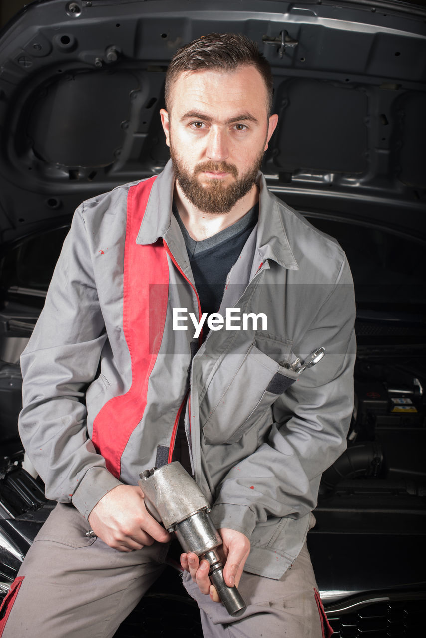 Portrait of male mechanic holding tool while sitting on chair