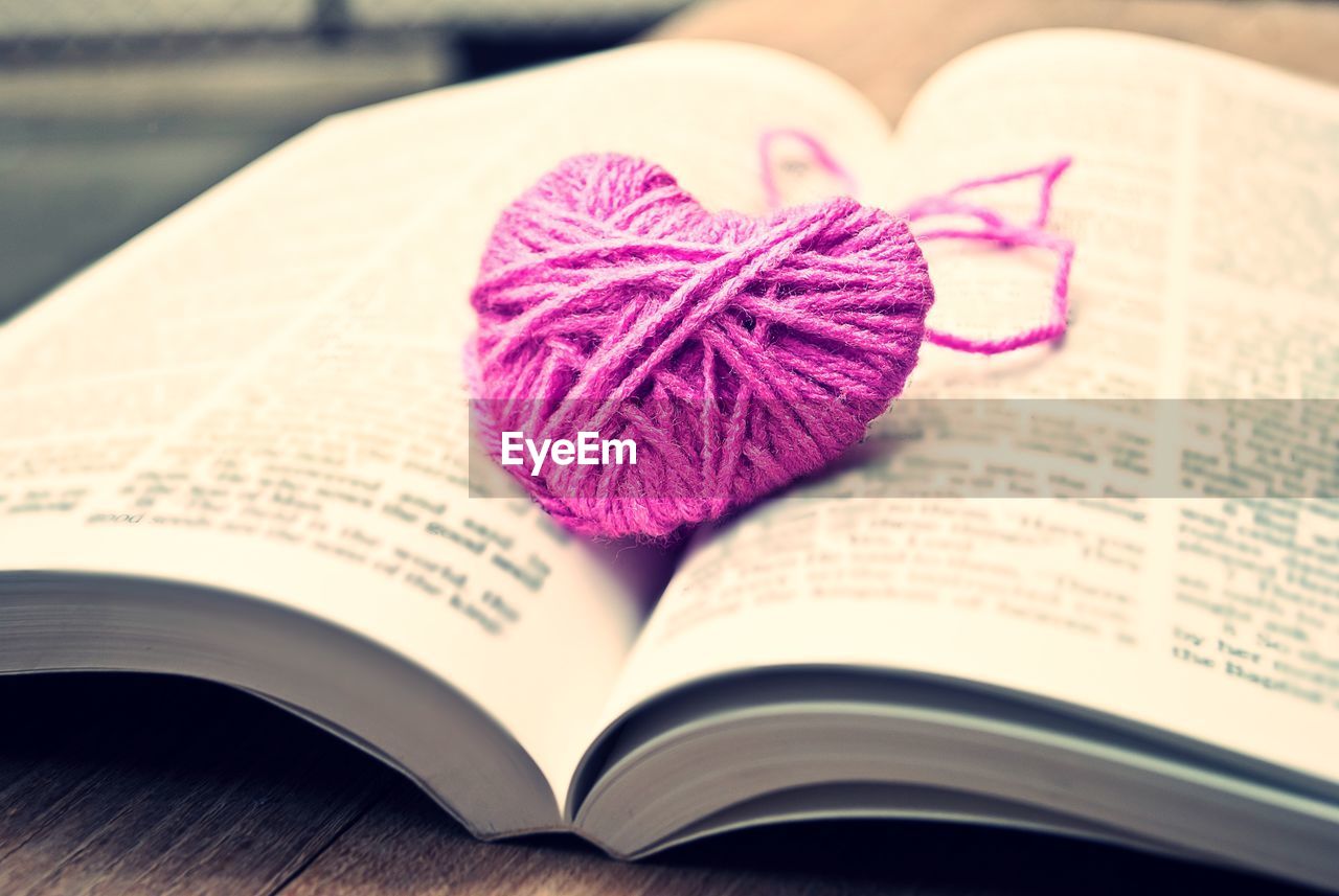 Close-up of knitted pink heart on open book