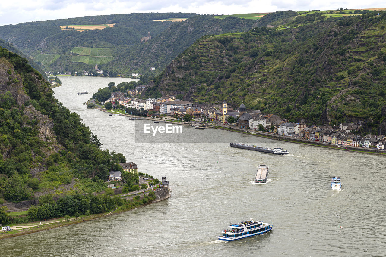 Tourist ships and barges sailing on the river rhine in western germany, visible buildings and hills.