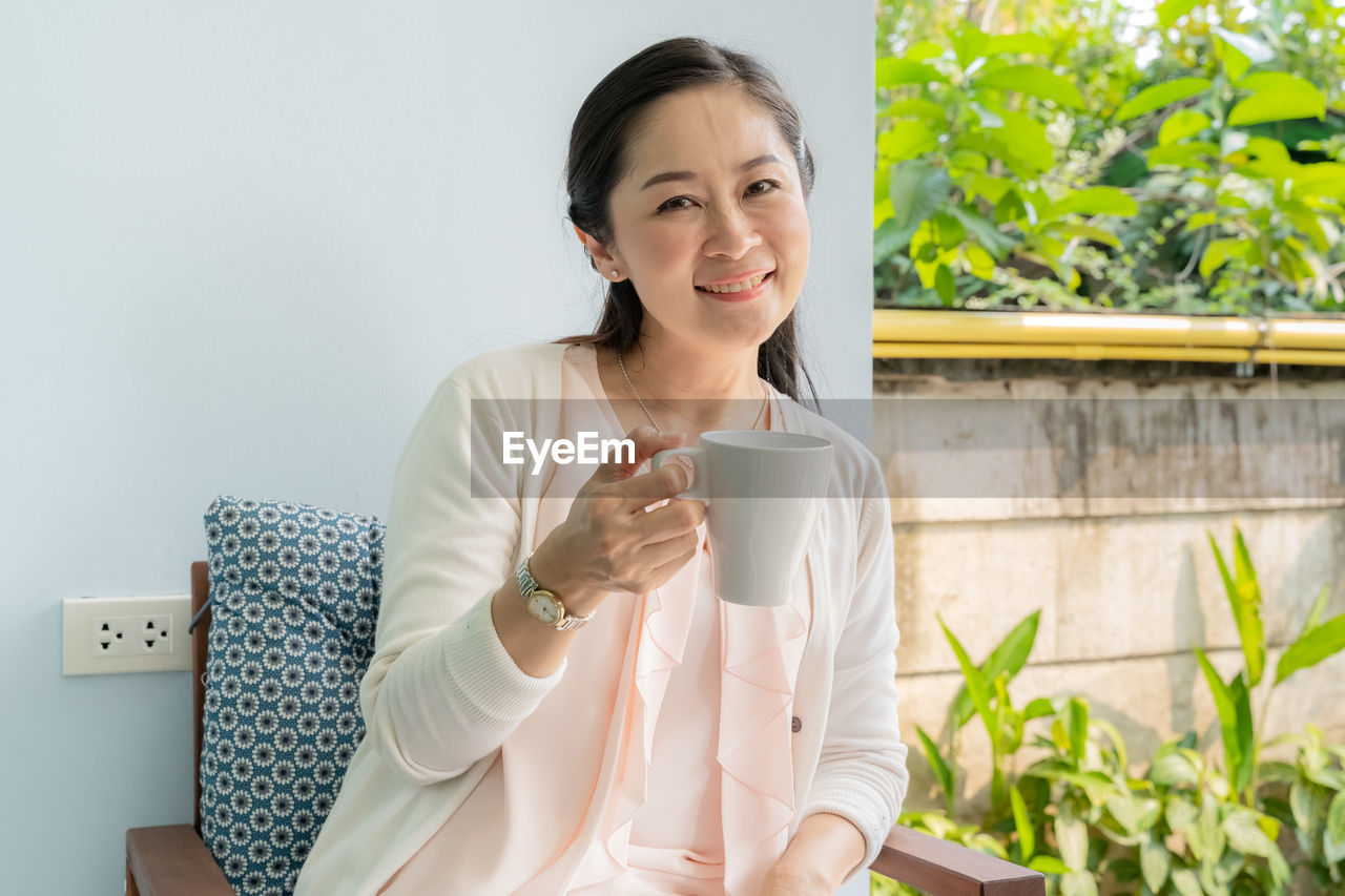 Smiling young woman holding coffee mug while sitting outdoors