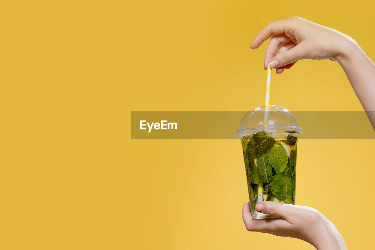 MIDSECTION OF WOMAN HOLDING GLASS OF YELLOW JUICE