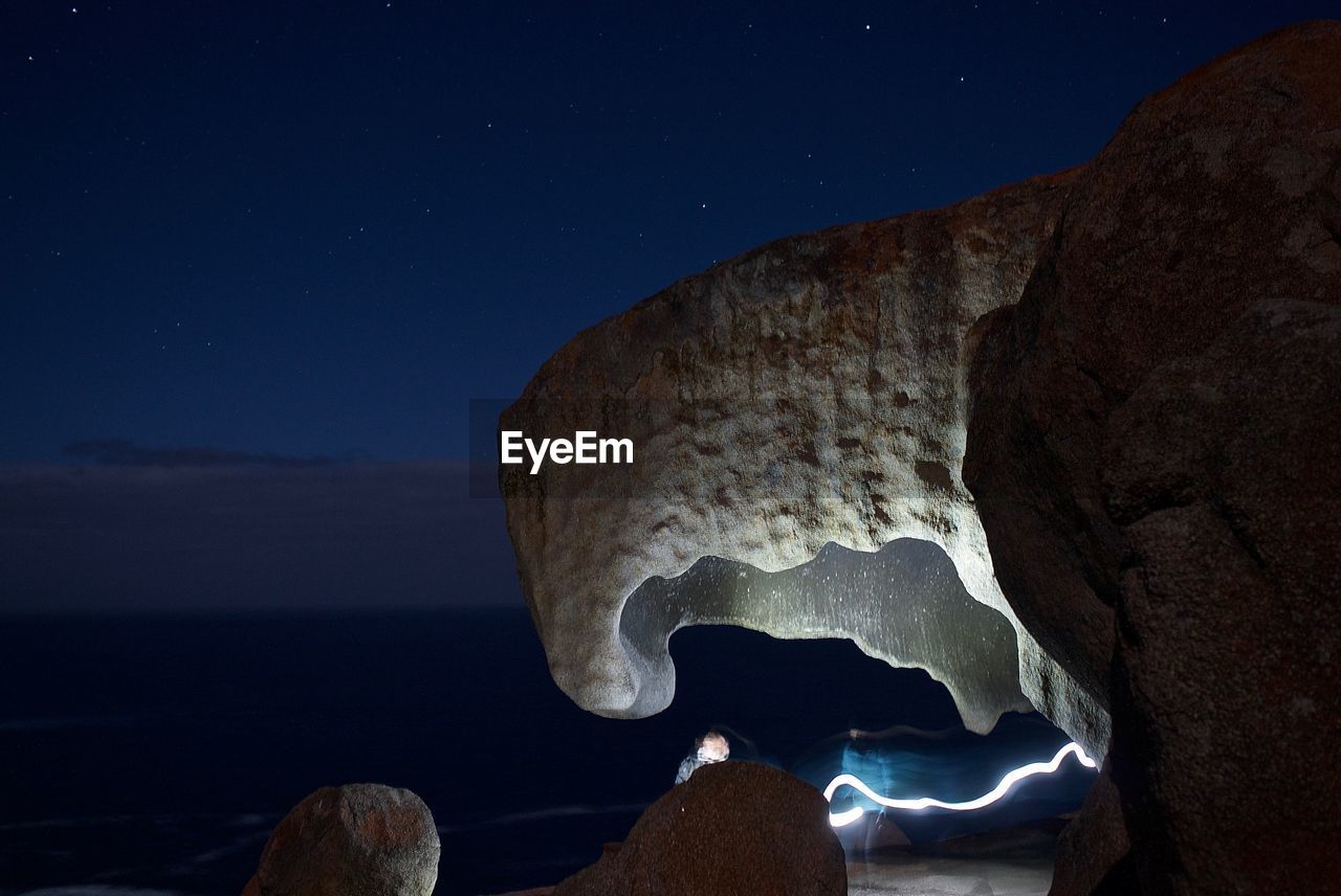 Rock formation by sea against sky at night