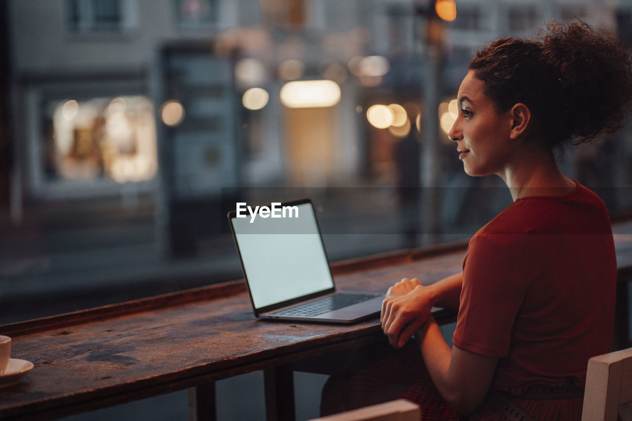 Young woman with laptop looking away while sitting by cafe table