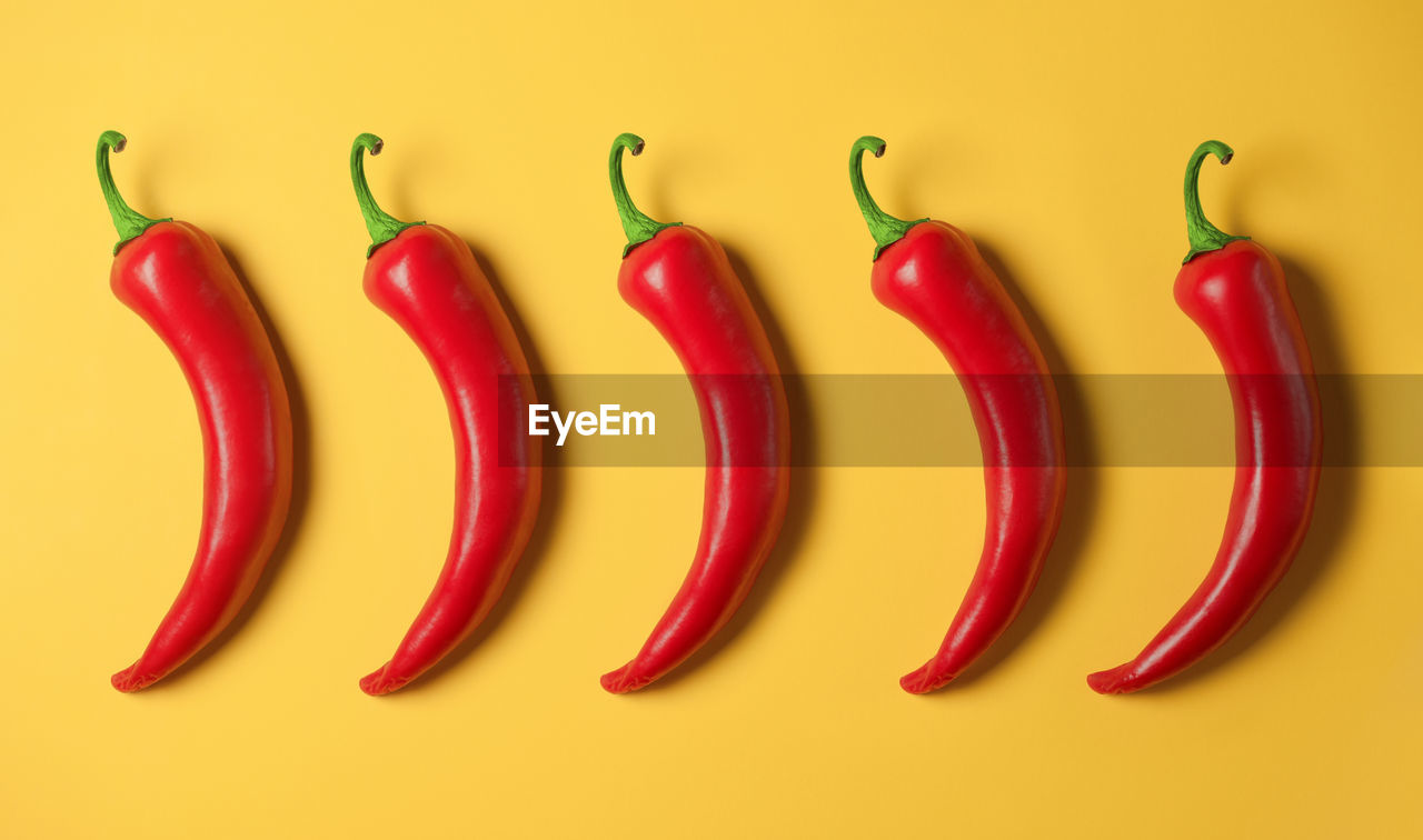 Five hot red peppers on a yellow background