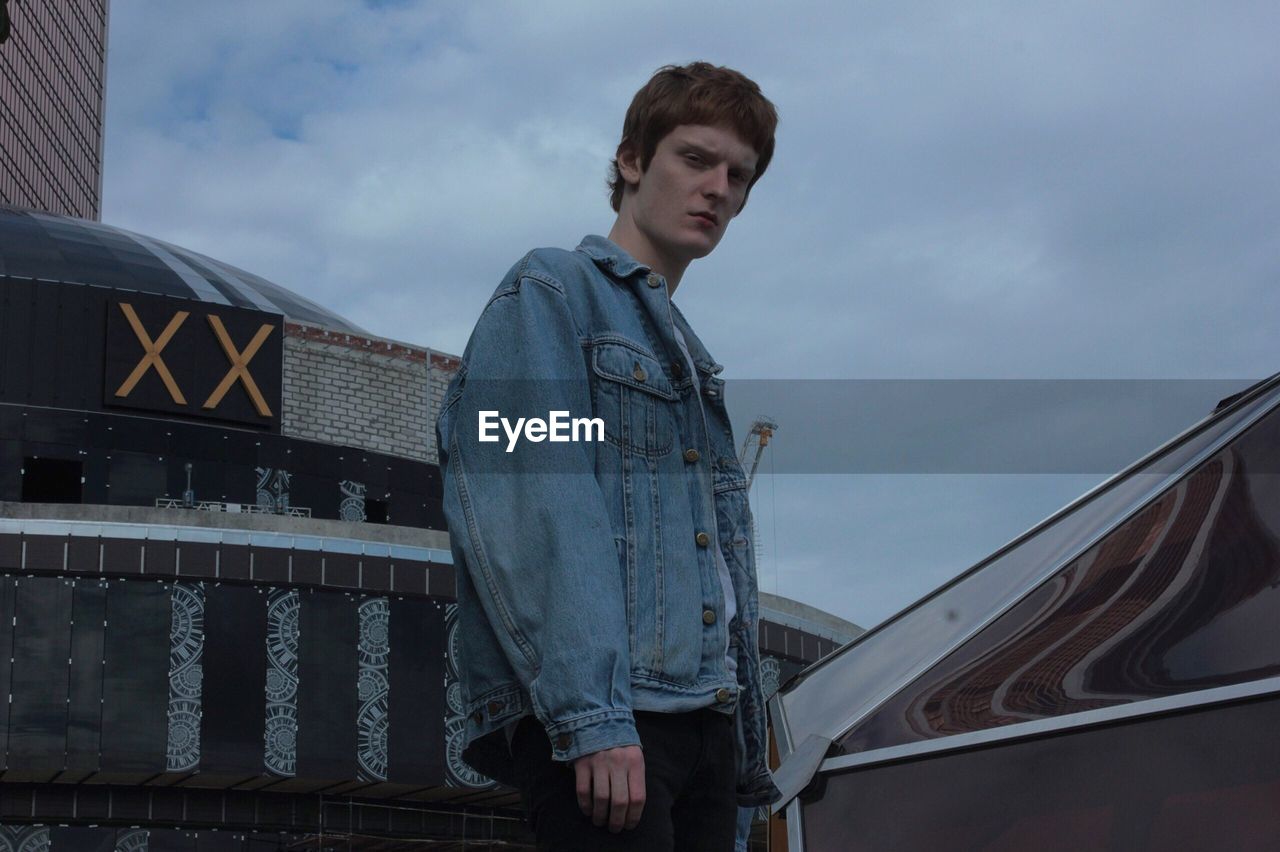 Low angle portrait of young man standing against cloudy sky