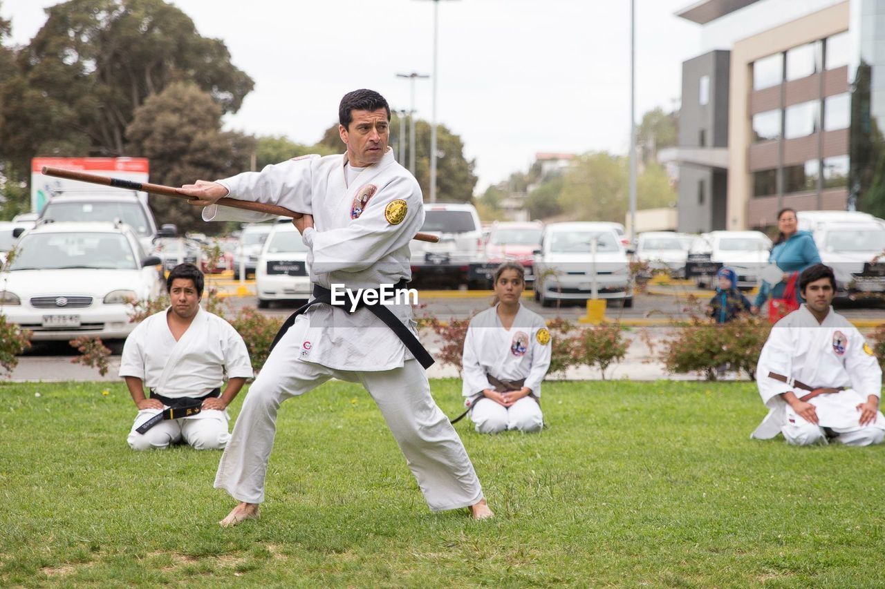 Full length of man practicing karate while students watching at park