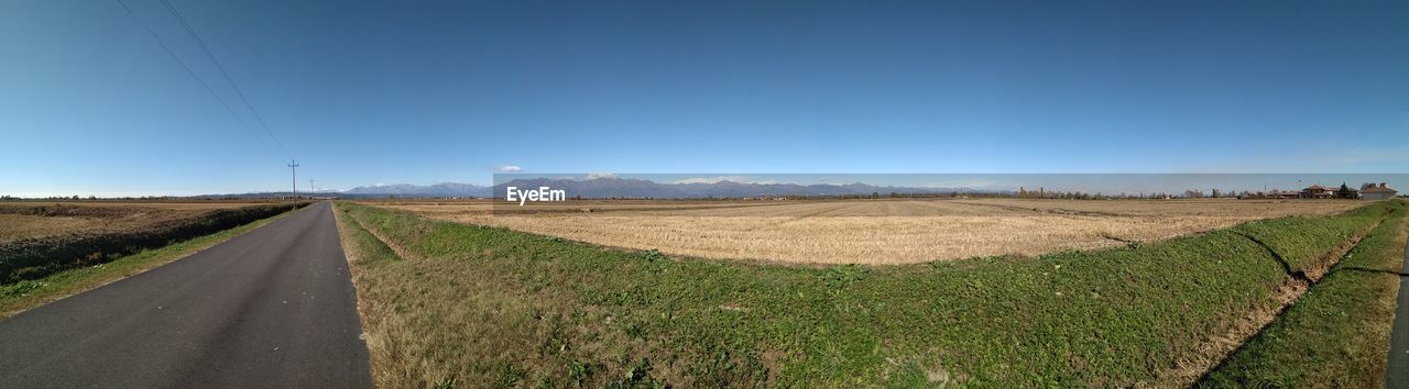 ROAD AMIDST AGRICULTURAL FIELD AGAINST CLEAR BLUE SKY