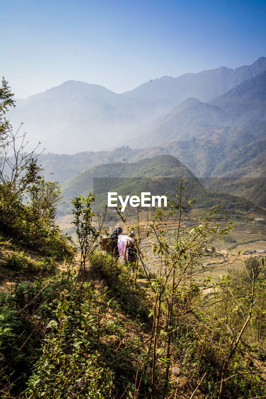 REAR VIEW OF PEOPLE ON LANDSCAPE AGAINST MOUNTAIN RANGE