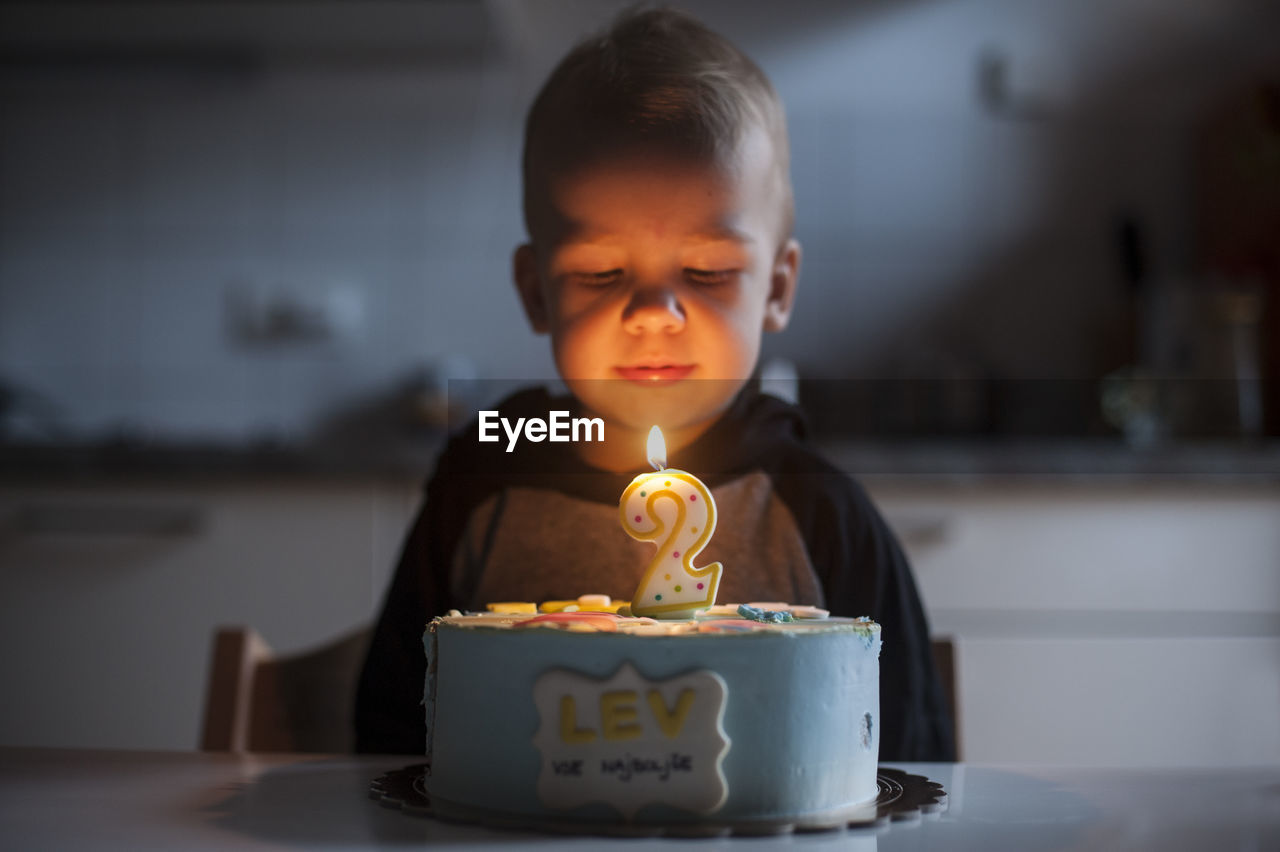Boy blowing candle on the birthday cake while celebrating his second birthday