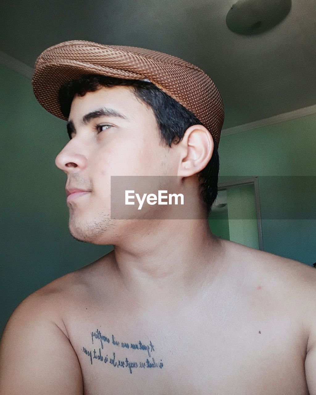 Close-up of shirtless young man wearing flat cap at home