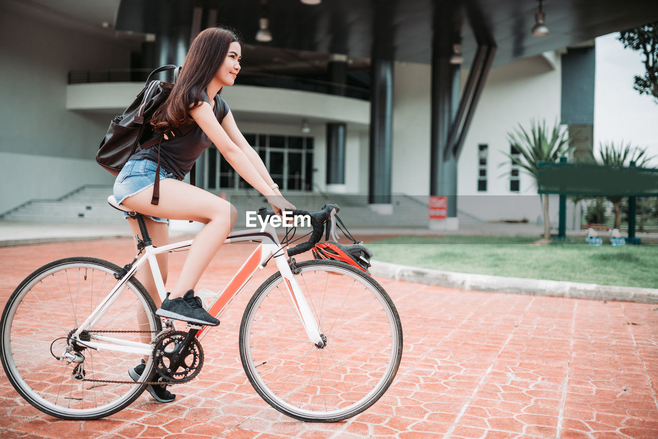 SIDE VIEW OF WOMAN RIDING BICYCLE ON A STREET