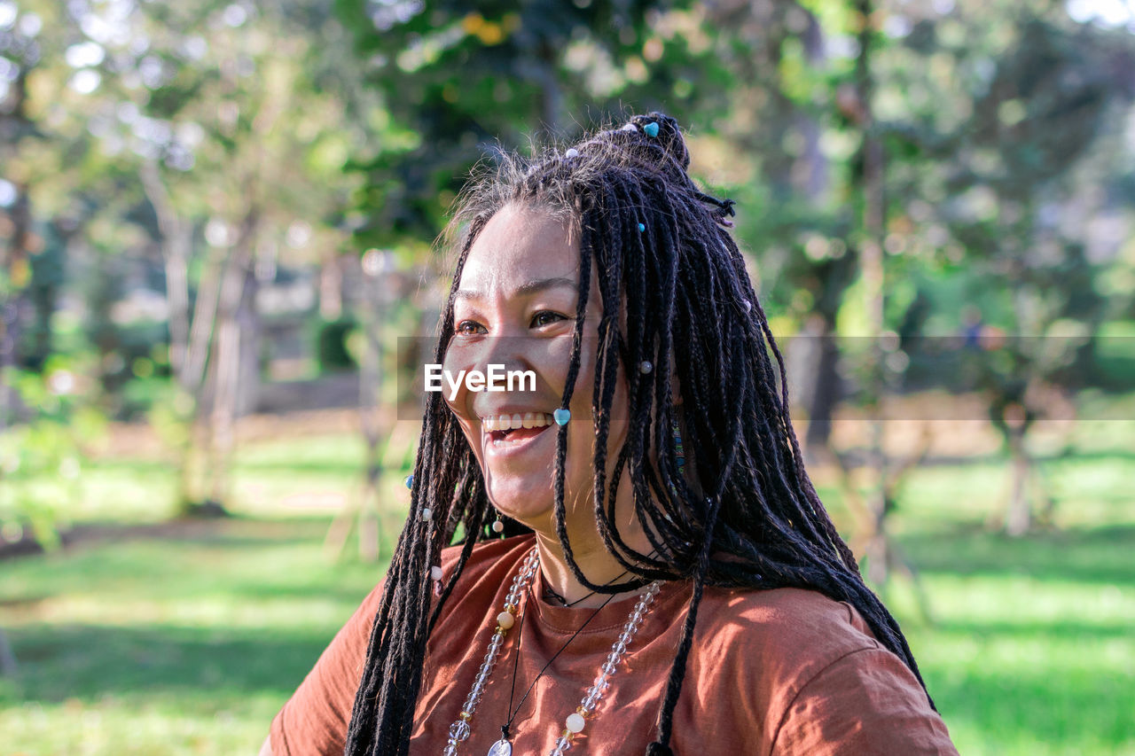 Portrait of beautiful woman with long african braids and ethnic decorations outside in a park.