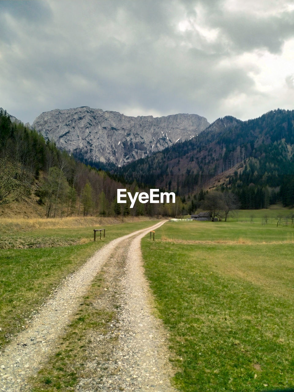 Dirt road amidst green landscape and mountains against sky