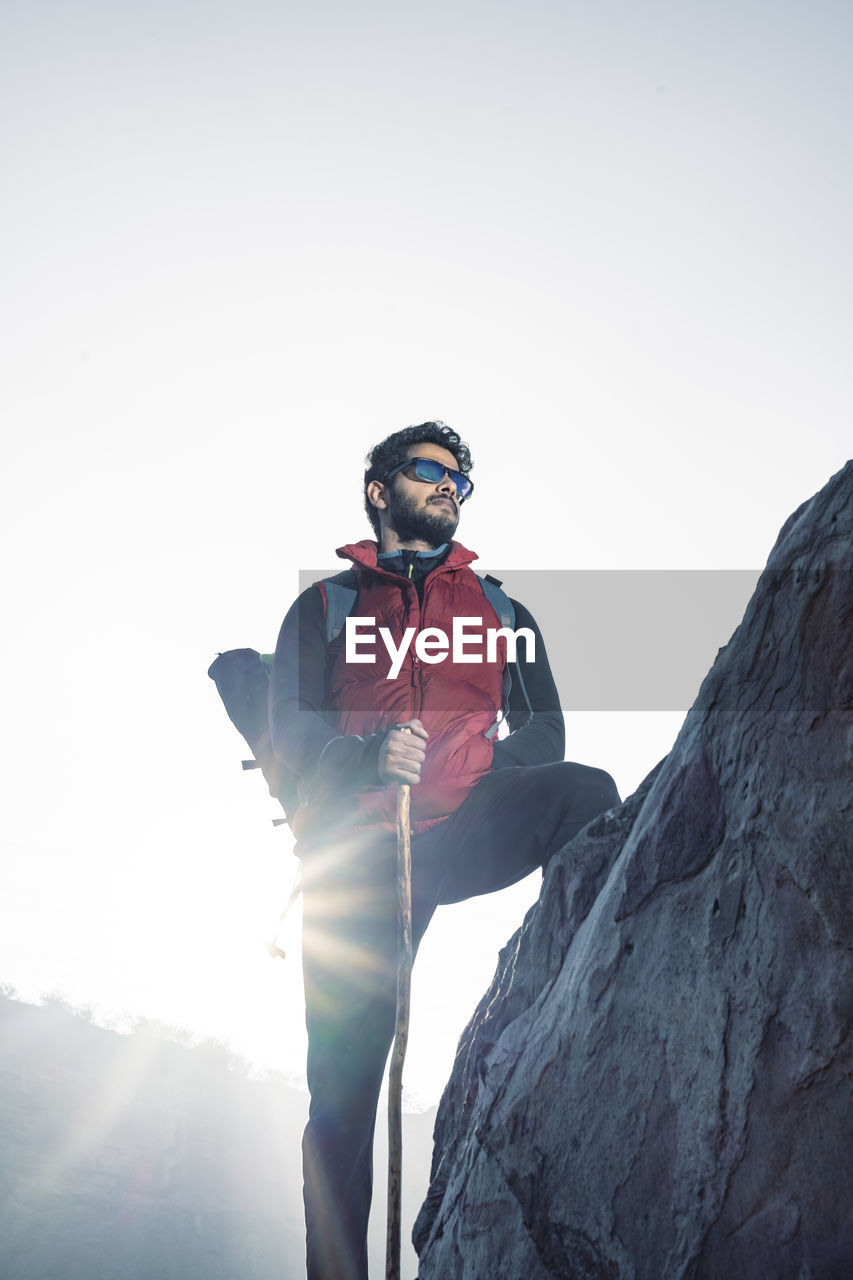 LOW ANGLE VIEW OF MAN STANDING ON ROCK