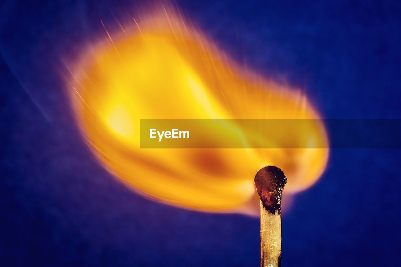 Close-up of burning matchstick head against blue background