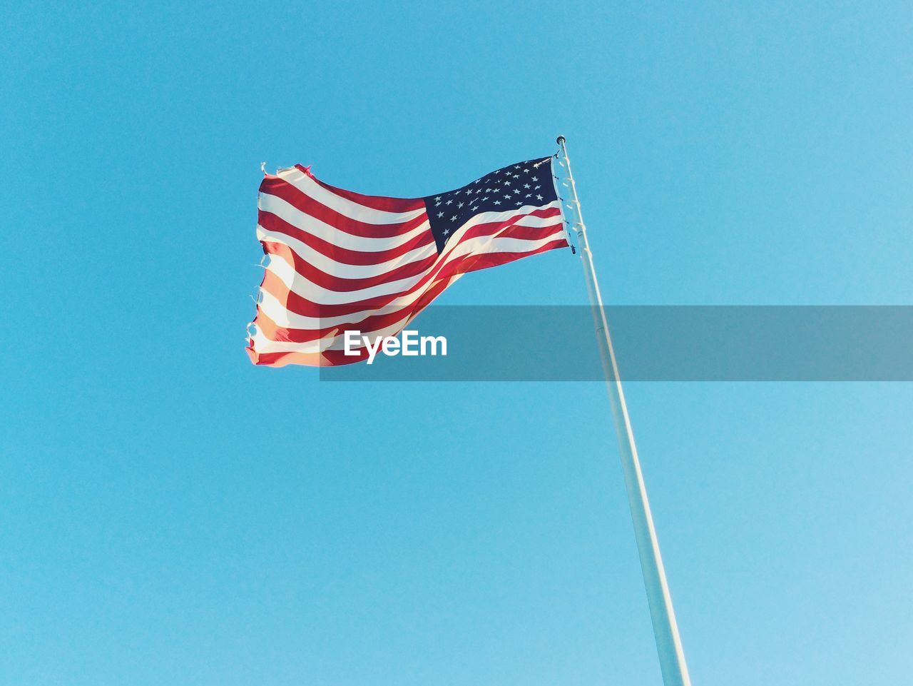 Low angle view of american flag waving against clear blue sky