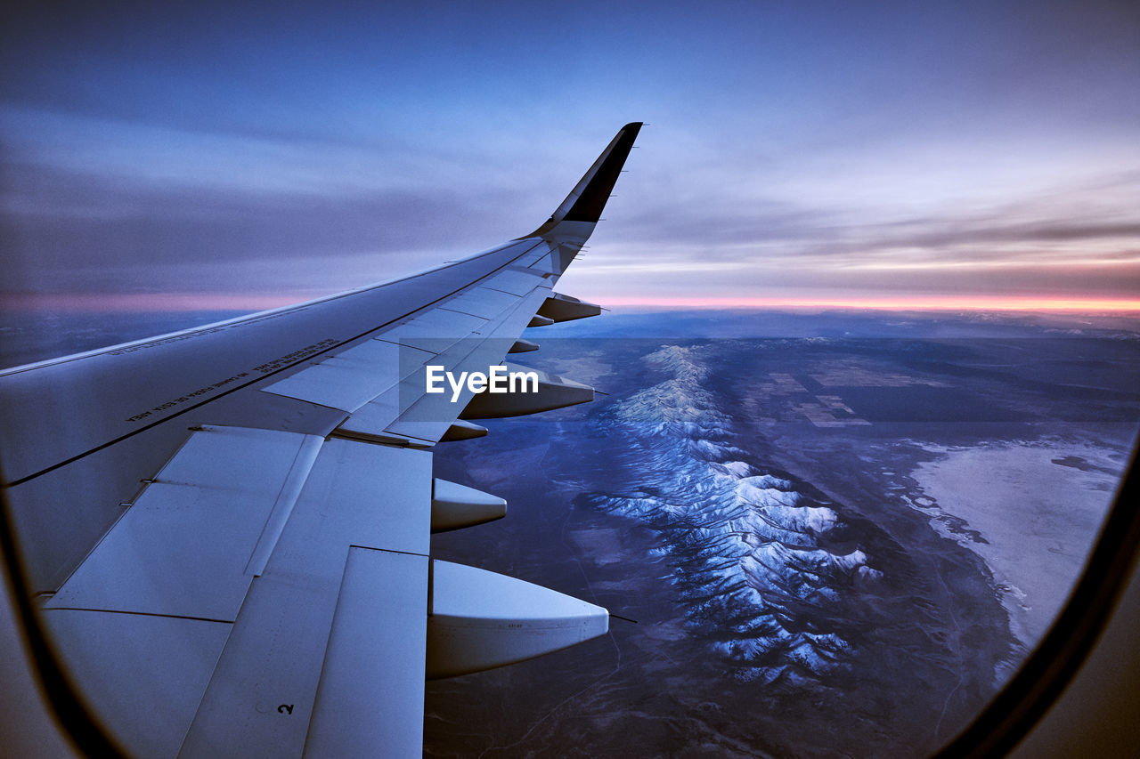 Airplane flying over landscape seen through window at sunset