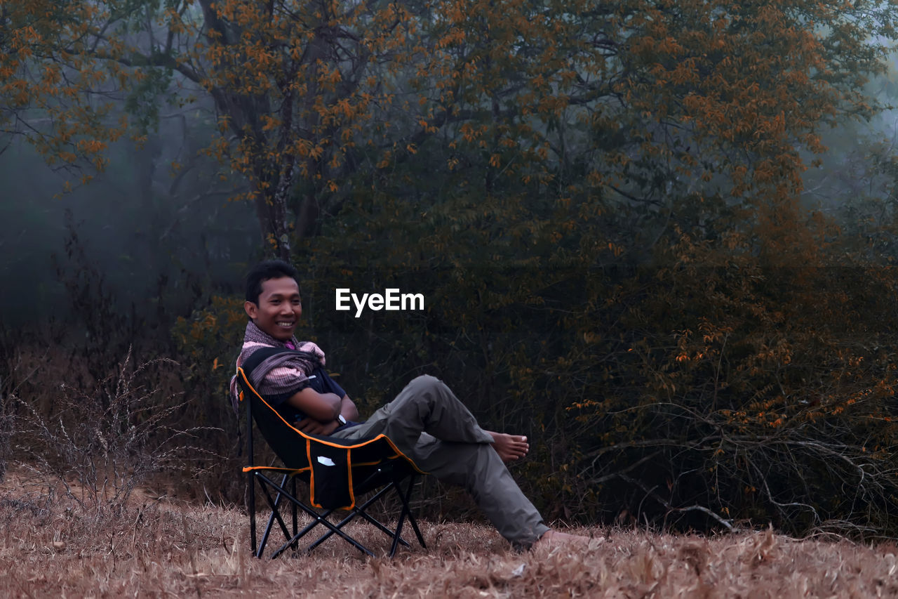 Portrait of young man sitting on chair in forest