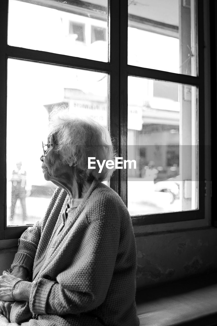 Old lady looking away while sitting on window at home