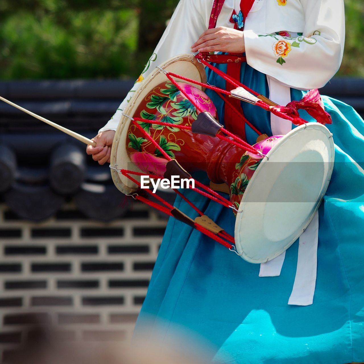 Midsection of woman in traditional clothes banging drum outdoors