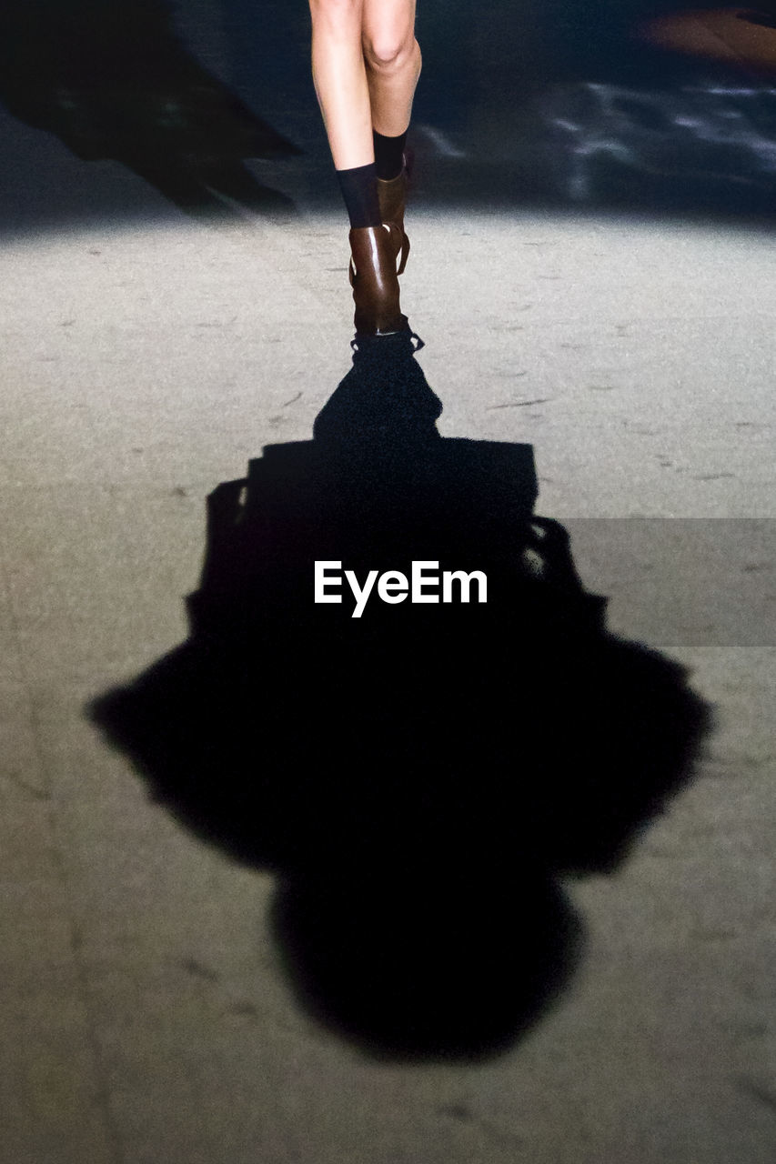 Low section of model on catwalk at fashion show with shadow