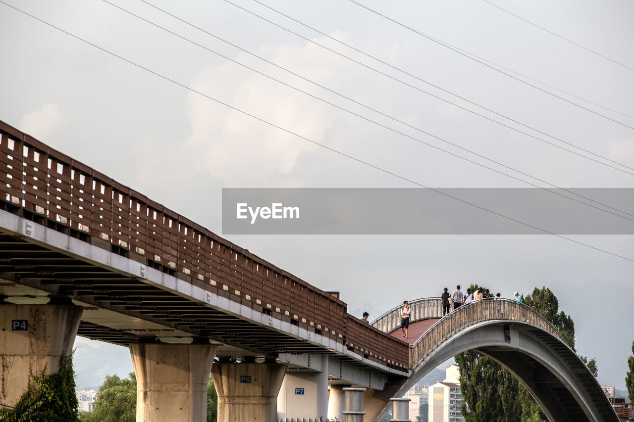 Low angle view of people walking on bridge against sky