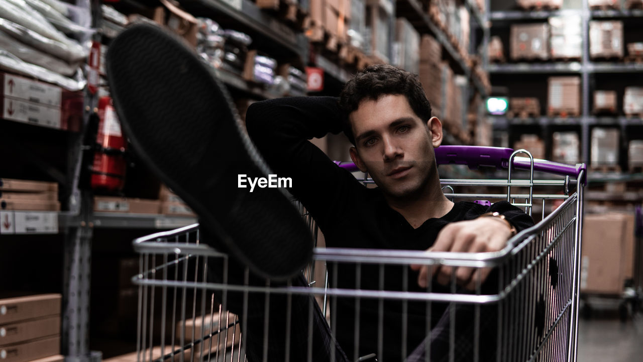 Portrait of young man sitting in shopping cart at store