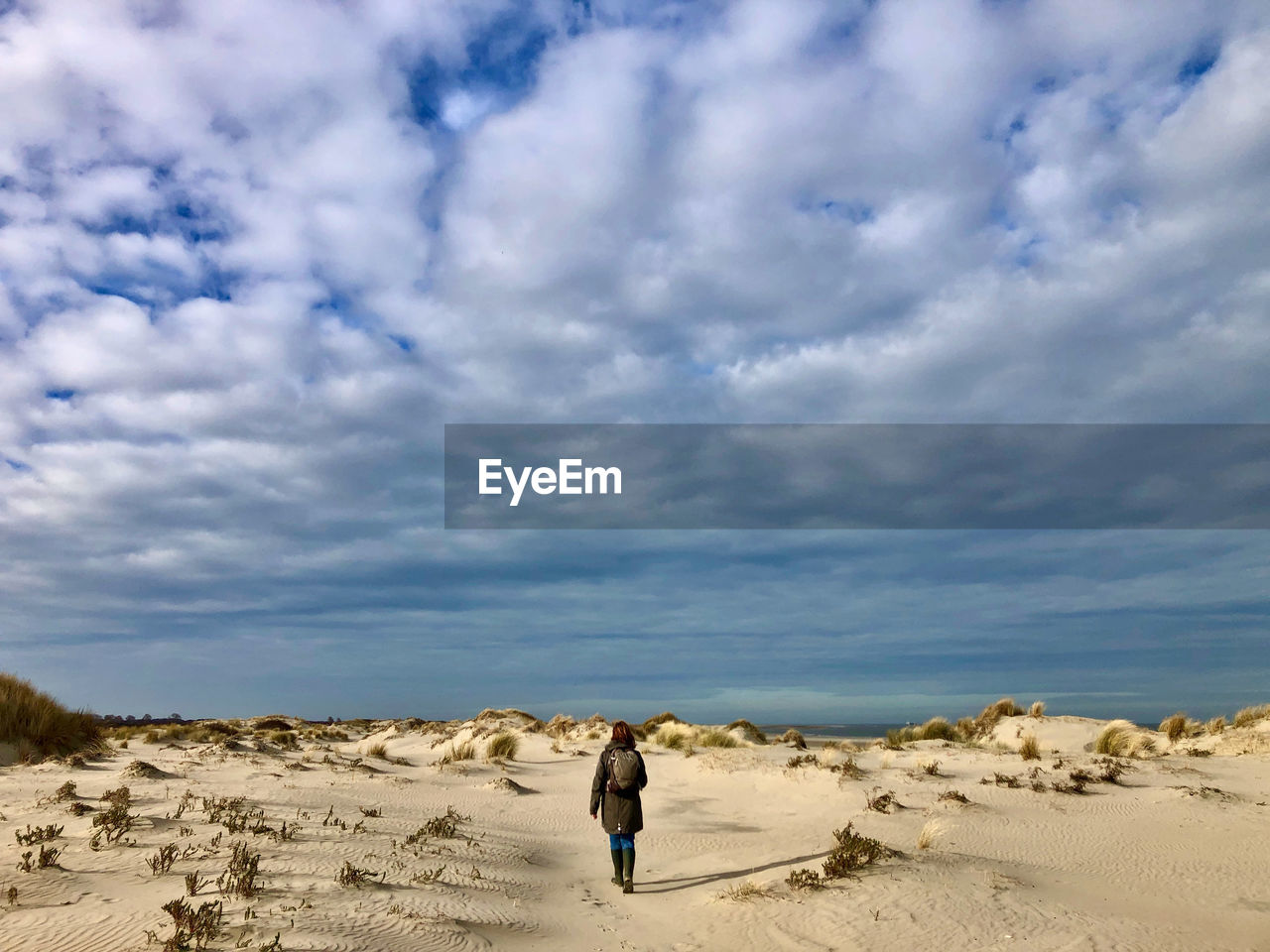 Rear view of woman amidst dunes against sky