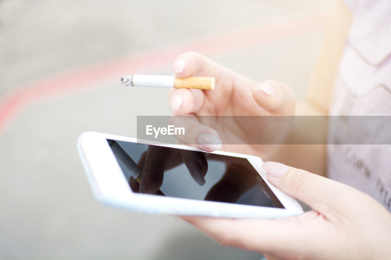 Midsection of woman using mobile phone while smoking cigarette