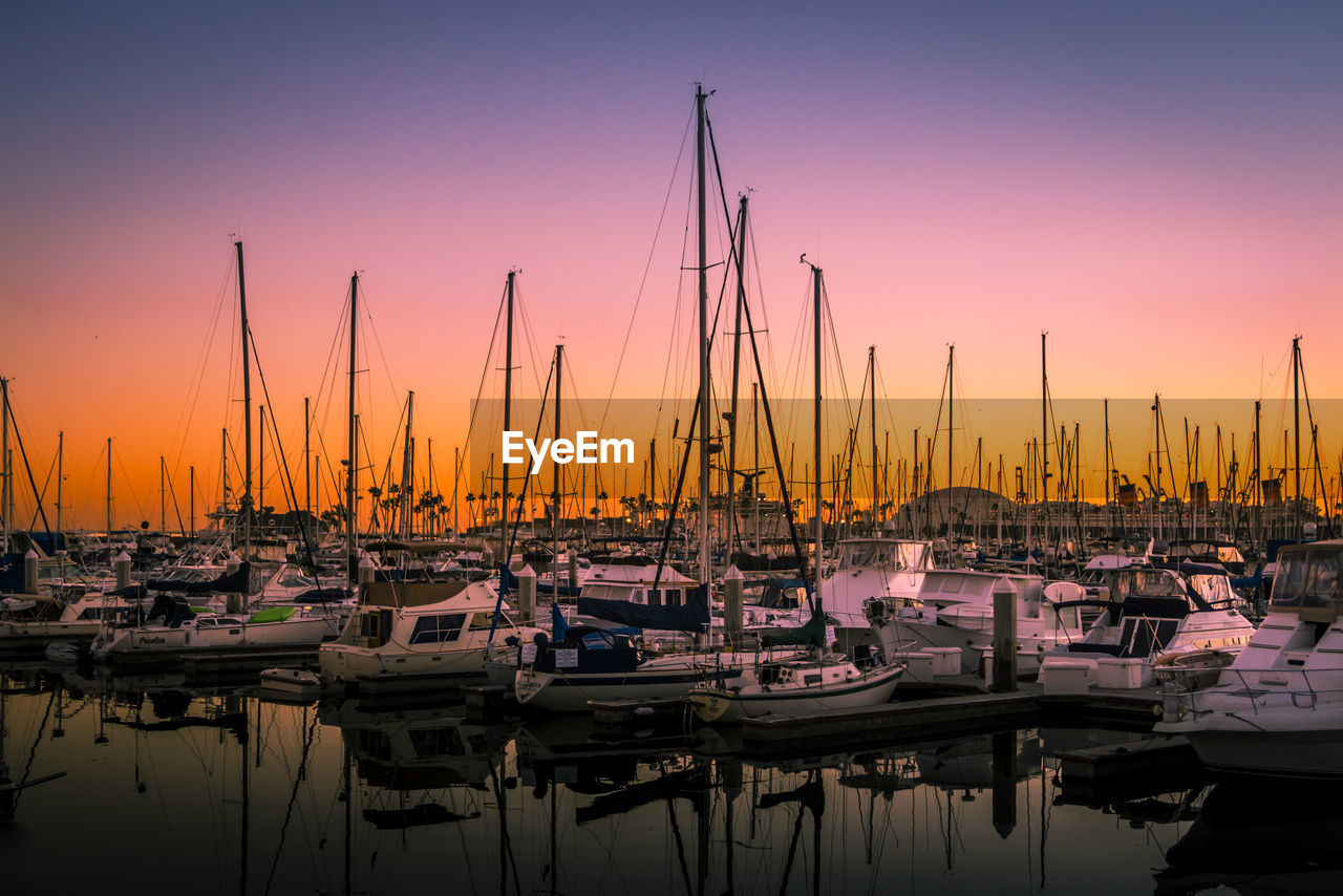 Boats moored at harbor against sky during sunset