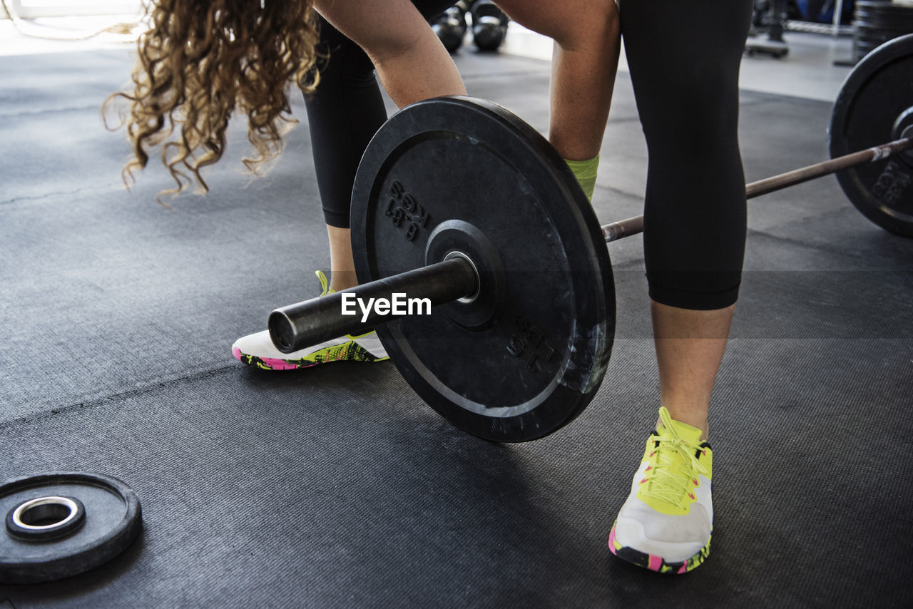 Midsection of woman exercising with barbell at crossfit gym